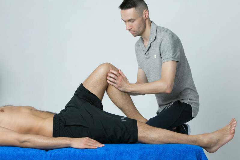 Overhead photo of physical therapy tools on a clean white surface: foam roller, resistance band set, handheld TENS unit, posture corrector, and soft massage ball